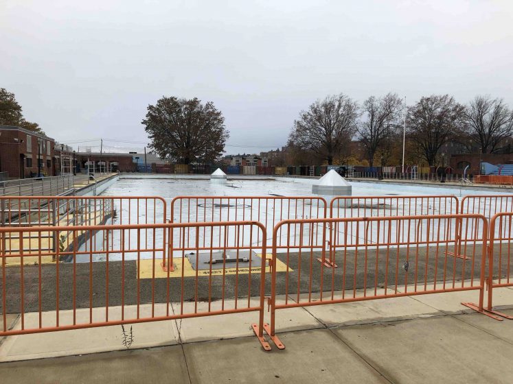 View of a large pool in Brookly, surrounded by orange metal fencing.